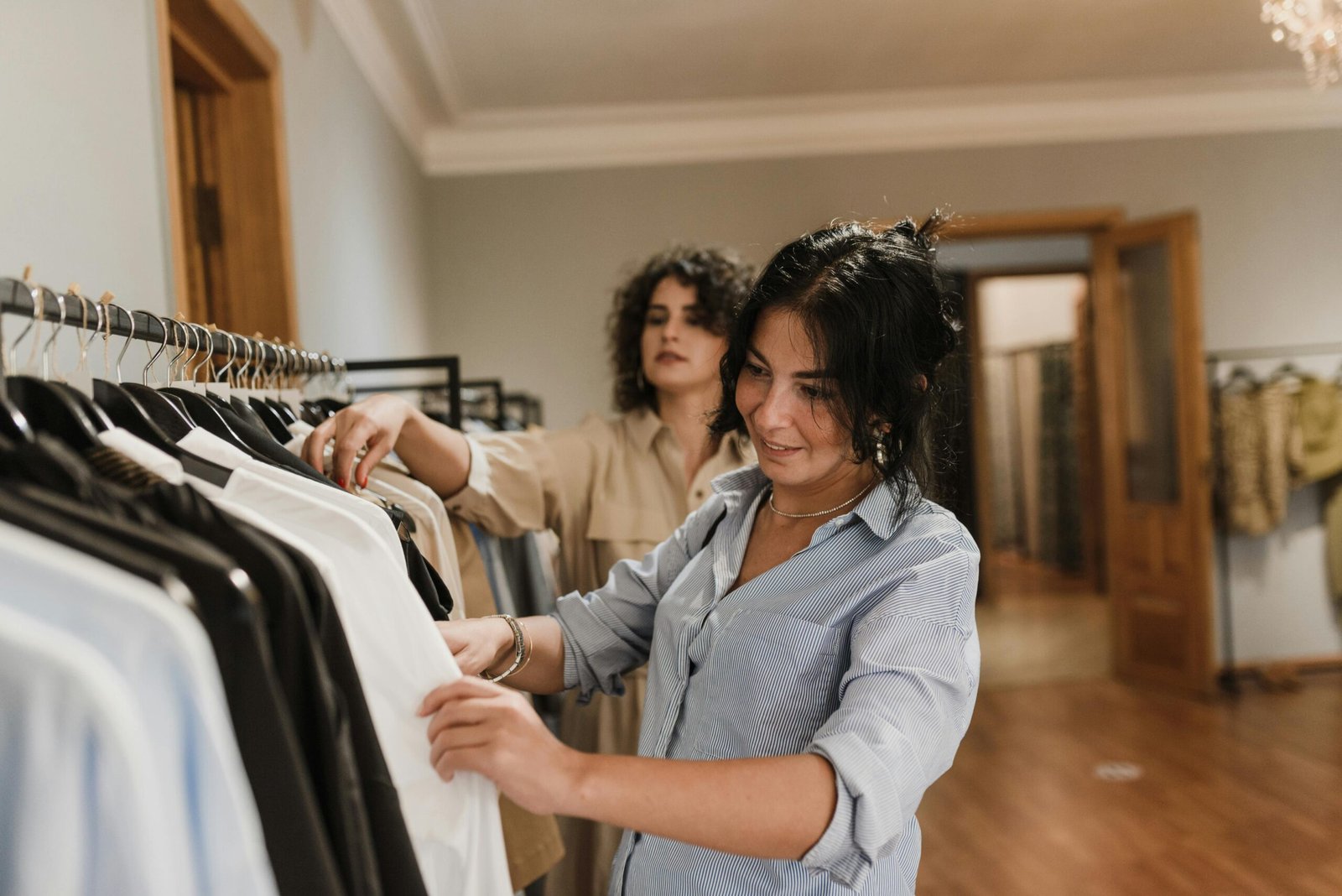 Two women browsing clothing racks together in an elegant boutique interior.